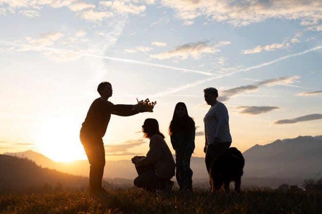 Couple standing together on a rock against a dramatic sunset, with one person presenting a small crown to the other, surrounded by a scenic landscape and mountains in the background, symbolizing a romantic and memorable anniversary trip.