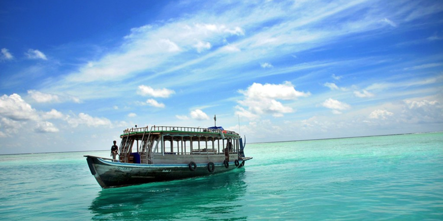 Maldives Travel Guide –  "Traditional Maldivian Dhoni boat sailing on crystal-clear turquoise waters under a bright blue sky, offering a serene island travel experience."