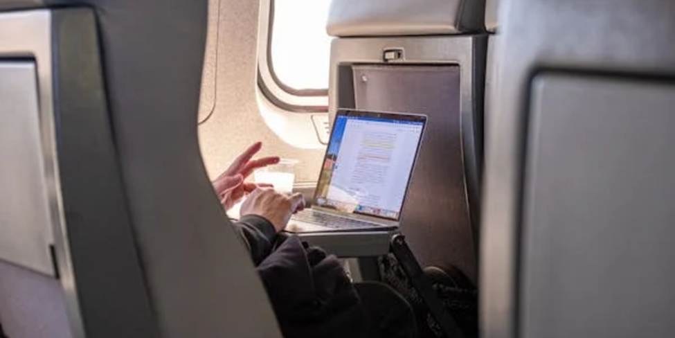 "Passenger working on a laptop in a spacious airplane seat, enjoying a comfortable business class travel experience."