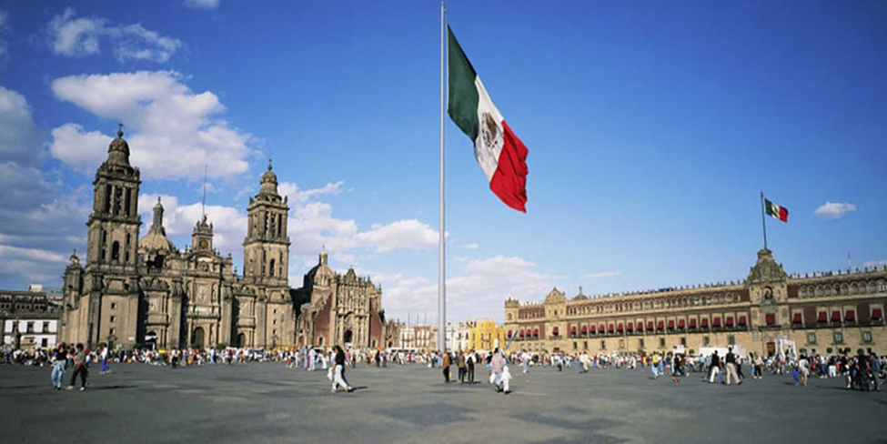 "Zocalo in Mexico City, a landmark in one of the dangerous cities in Mexico, featuring the Metropolitan Cathedral, National Palace, and a large Mexican flag."