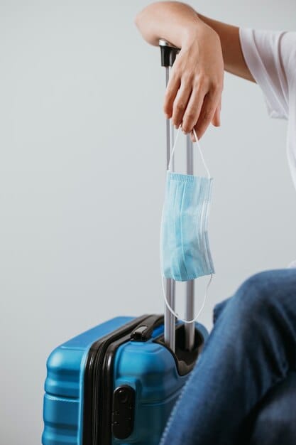 Traveler with a blue suitcase holding a disposable face mask, highlighting the importance of carrying protective gear like face masks during travel