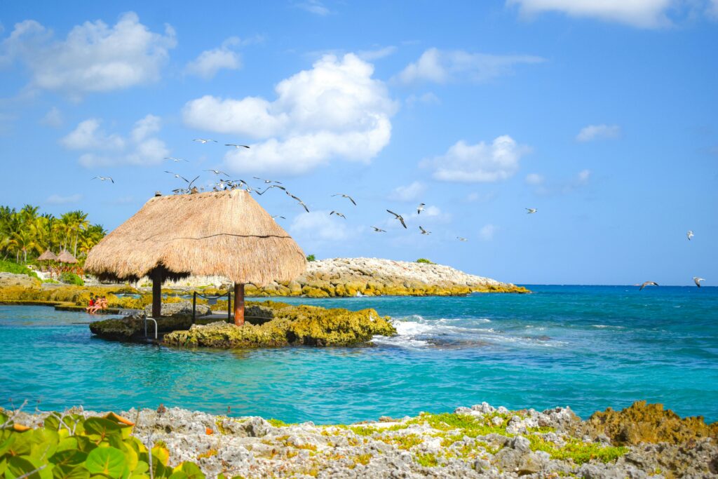 Idyllic tropical beach scene with a thatched hut, azure waters, and clear skies.