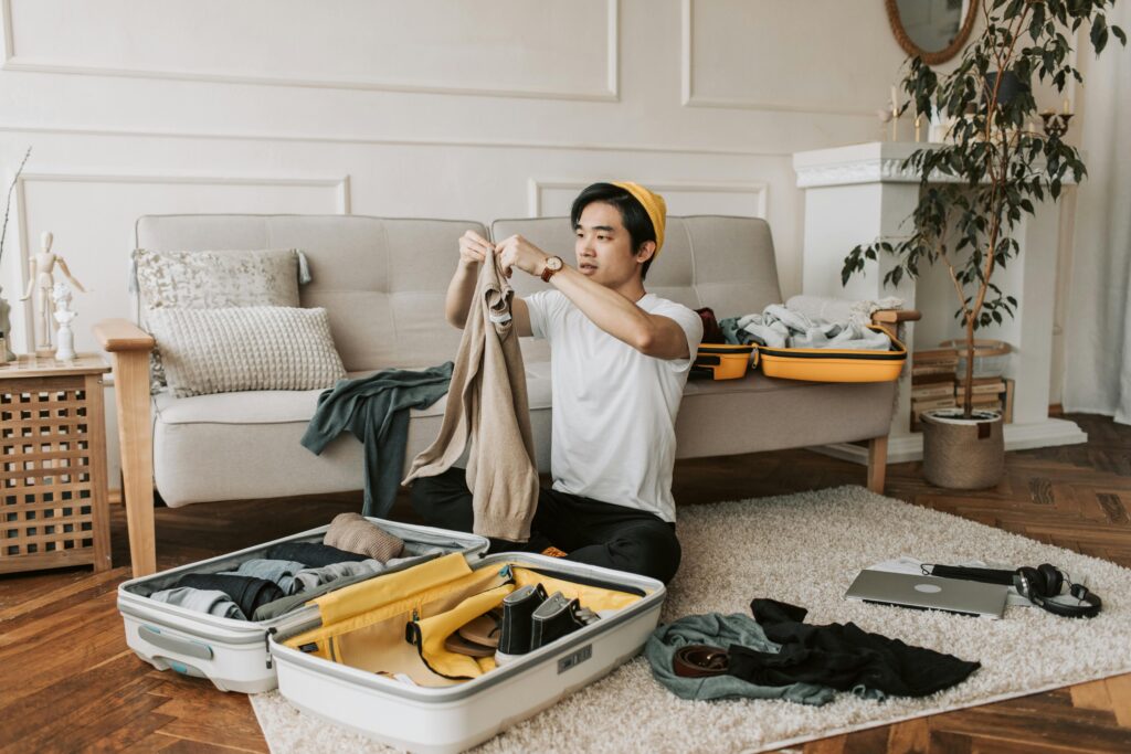 A young man organizes clothes into a suitcase in a stylish living room, preparing for a trip.