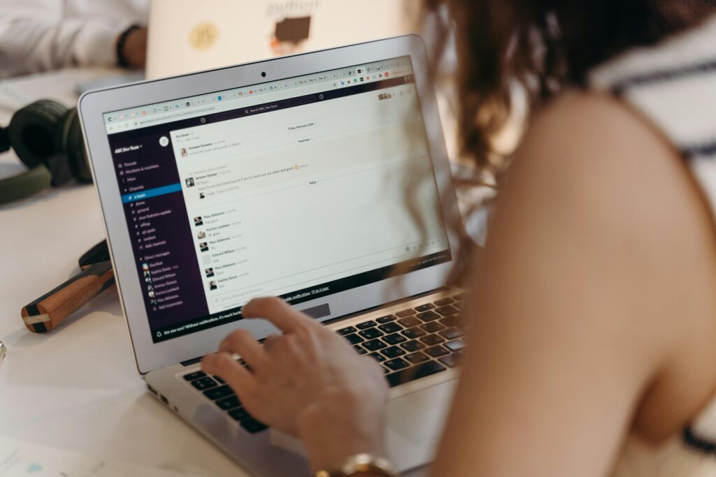 A businesswoman typing on a laptop in an office setting, using Slack for communication.